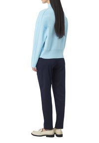 Hellblau gestrickter Pullover mit hohem Kragen und geripptem Saum, kombiniert mit dunkelblauen, taillierten Hosen und hellen Loafers.