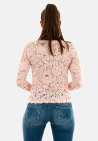 Maglioncino rosa in pizzo con motivo floreale, maniche lunghe e collo rotondo. Indossato sopra jeans in denim blu con tasche posteriori visibili.