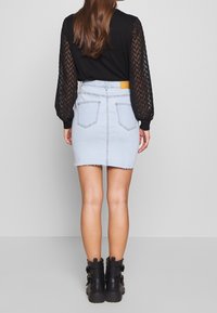 Ljusblå denim mini kjol med fransad fåll, i kombination med en svart topp med texturerade, genomskinliga, mönstrade ärmar. Svarta ankelstövlar ingår.