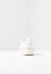 Baskets blanches avec un dessus en cuir lisse, profil bas, bout rond et design minimaliste. Présentent un accent subtil en or près de la semelle.