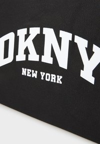 Sac en tissu noir avec le texte blanc "DKNY" et "NEW YORK" en lettres courbes et en gras ; surface texturée ; design minimaliste.