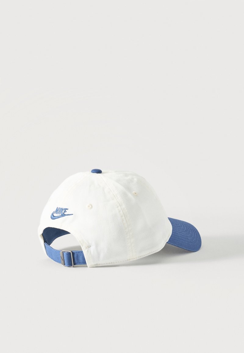 Weißes Nike Baseballcap mit blauem verstellbarem Riemen und blauem gebogenem Schirm, von hinten vor weißem Hintergrund gezeigt.