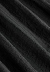 Schwarzer Stoff mit einem strukturierten, diagonalen Rippmuster. Der Stoff fällt in sanften Falten und zeigt eine reiche, tiefe Farbe sowie eine glatte Oberfläche.