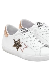 Sneakers bianchi con dettagli metallici in oro rosa sul tallone, caratterizzati da un design di stelle nere e glitterate sul lato. Suola in gomma testurizzata.