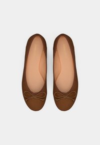 Ballerines en tissu marron avec une surface texturée, un bout arrondi et un nœud décoratif sur le devant. Doublure intérieure rose pâle.