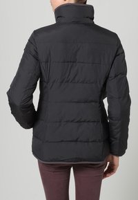 Svart puffjacka med hög krage, quiltad textur och figursydd design. Slätt material utan synlig hårdvara eller dekorationer.