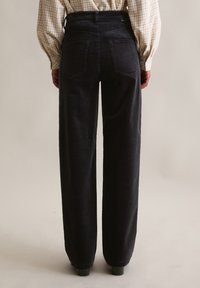 Zwarte corduroy broek met wijde pijpen, hoge taille, zichtbare achterzakken en een gestructureerde afwerking. Ontworpen voor een ontspannen pasvorm.