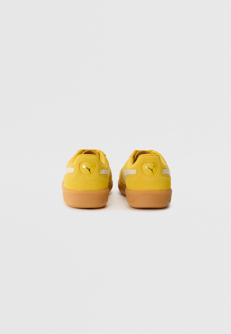 Gelbe Wildleder-Sneaker mit strukturiertem Finish, ausgestattet mit einer Gummisohle, weißen Streifen an den Seiten und einem erhabenen Logo auf der Rückseite.