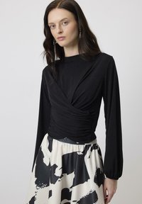 Black long-sleeve top with gathered front detail paired with a flowing beige skirt featuring a bold black abstract pattern.