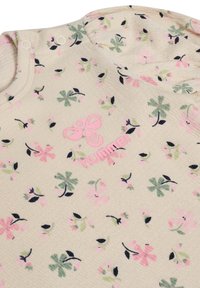 Lys beige bomuldsbeklædning med et blomsterprint i pink og grøn, med et pink "hummel" logo og trykknapper på skulderen.