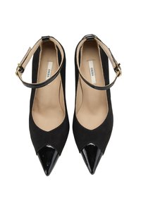 Chaussures à talons hauts noires avec un bout pointu, fabriquées en daim et en cuir verni. Elles comportent une bride de cheville avec une boucle dorée.