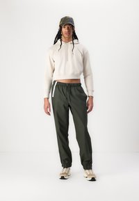 Cropped beige hoodie, green drawstring pants, and beige sneakers with black soles. Cap features a camouflage pattern and a curved brim.
