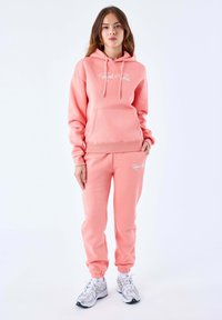 Roze hoodie en bijpassende sweatpants van een katoenmix; beschikt over een voorzak, verstelbare trekkoorden en geribbelde boorden.