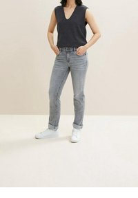 Top gris sin mangas con escote en V, combinado con jeans gris claro con puños doblados y zapatillas blancas, sobre un fondo neutro.