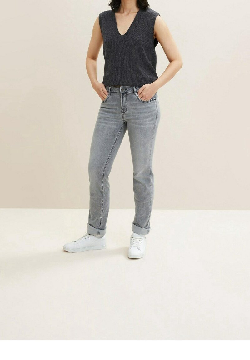 Top gris sin mangas con escote en V, combinado con jeans gris claro con puños doblados y zapatillas blancas, sobre un fondo neutro.