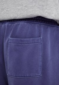 Violetās sporta bikses ar sānu kabatu, elastīgu jostasvietu un mīkstu, teksturētu audumu. Jostasvieta ir savilkta komfortam.