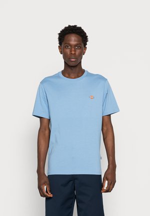 T-shirt de algodão azul claro com decote redondo e mangas curtas, apresentando um pequeno logotipo bordado no lado esquerdo do peito. Textura suave.