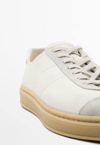 Weiße Leder-Sneaker mit grauem Wildlederbesatz, runder Form, Schnürdesign und strukturiertem beigen Gummisohle.