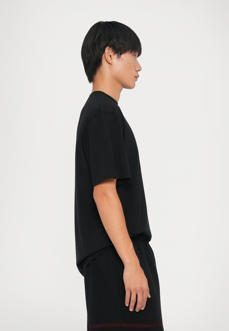 Sort kortærmet t-shirt i en afslappet pasform, lavet af bomuld, med en glat tekstur. Parret med matchende shorts med røde syninger.