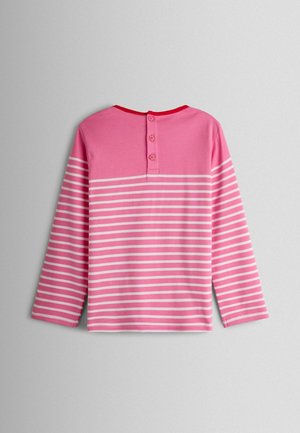 Tričko s dlhými rukávmi v ružovej farbe s vodorovnými bielymi pruhmi. Má zaoblený výstrih s červeným lemom a tri gombíky na zadnej strane.