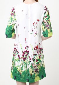 Vestido floral con base blanca y patrones de plantas en verde y morado. Mangas cortas y abullonadas en un acento verde. Cierre en la parte trasera con botones.