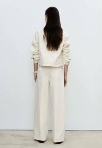 Cream-colored denim jacket with puffed sleeves paired with wide-leg cream trousers. Smooth texture, minimalist design, no visible hardware.