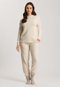Cremfarbener Fleece-Loungewear-Set, bestehend aus einem Langarmoberteil mit Rundhalsausschnitt und tapered Hosen mit elastischen Bündchen.