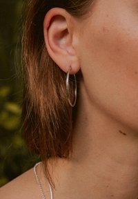 Silberne Creole, die in einem gepiercten Ohr getragen wird. Die Ohrringe haben eine glatte, reflektierende Oberfläche und zeigen ein klassisches, kreisförmiges Design.