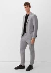 Hellegrauer, strukturierten Anzug mit schmaler Passform, bestehend aus einem einreihigen Blazer, klaren Linien und Taschen, kombiniert mit schwarzen Sneakers.