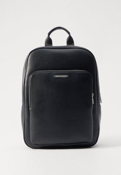 Sac à dos en cuir noir avec une finition texturée, poche zippée à l'avant et poignée supérieure. Comprend un détail de logo argenté et des accents de fermeture éclair lisse.