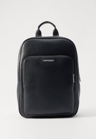 Sac à dos en cuir noir avec une finition texturée, poche zippée à l'avant et poignée supérieure. Comprend un détail de logo argenté et des accents de fermeture éclair lisse.