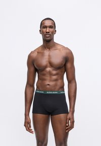 Μαύρα βαμβακερά σλιπάκια με πράσινη ζώνη που φέρει το λογότυπο "BJÖRN BORG". Λείος υφασμάτινος σχεδιασμός, εφαρμοστός και μήκος μέχρι το μέσο μηρό.