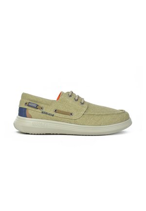 Zapatillas de lona verdes con suela de goma, que cuentan con ojales de metal, un acento naranja y un detalle en el talón en azul y marrón.