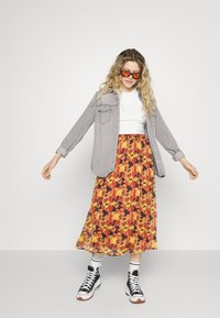 Grijze knoopshirt, witte getailleerde t-shirt, en een bloemen midi rok in oranje en gele tinten. Zwarte hoge sneakers met witte veters.