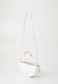 Vit handväska med en böjd design, guldfärgade beslag och en flätad detalj av naturfiber på toppen. Har en lång axelrem och en tofsdetalj.