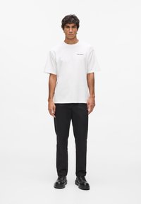 Biela bavlnená tričko s okrúhlym výstrihom a krátkymi rukávmi, skombinované s čiernymi nohavicami a čiernymi topánkami. Jednoduchý dizajn, bez viditeľných vzorov.