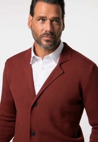 Bordeaux pletený cardigan s texturovaným povrchem, s jednoduchým zapínáním na knoflíky, s černými knoflíky, nošený přes bílou košili s límcem.