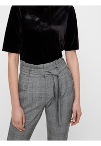 Haut noir en velours à manches courtes associé à un pantalon taille haute à carreaux gris, avec un détail de ceinture nouée et un tissu texturé.
