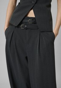 Sötétszürke csíkozott öltöny, testre szabott mellénnyel és laza nadrággal. Két fekete öv fémcsatokkal és mély oldalzsebek jellemzik.