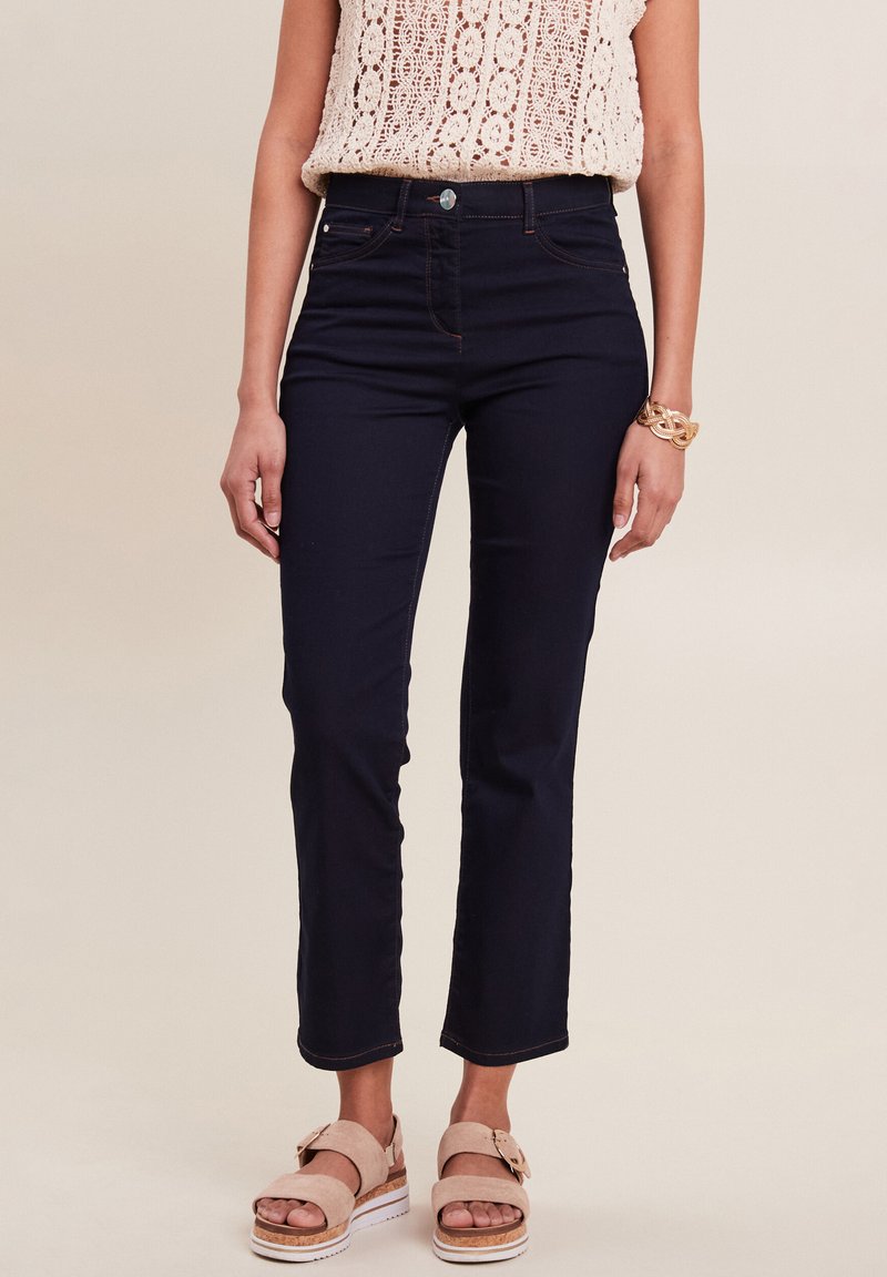 Donkerblauwe denim jeans met een slimfit ontwerp, voorzien van vijf zakken, riemlussen en een iets verkorte lengte. Gepaard met lichtroze sandalen.