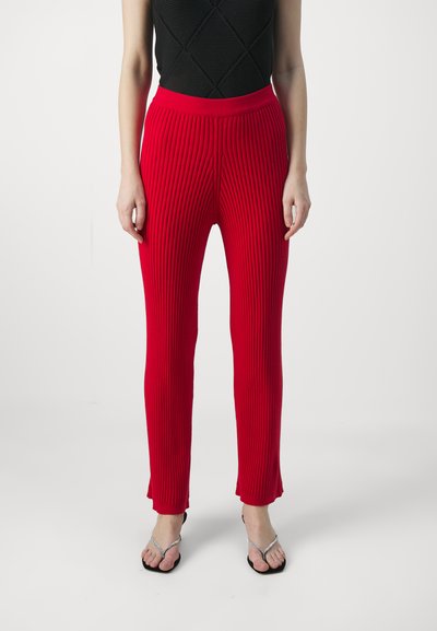 Rote gerippte Strickhose mit einem schmalen Bund, ausgestattet mit einem schmal zulaufenden Beinschnitt. Die Textur ist glatt mit vertikalen Rippendetails.