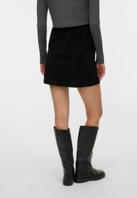 Jupe mini en velours côtelé noir avec une taille élastique, associée à des bottes en cuir noir montant jusqu'aux genoux et un haut gris à côtes ajusté.