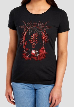 Woman wearing black t-shirt with red and black graphic of a demonic face, lightning, and a figure wielding a weapon, paired with blue jeans.