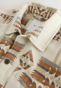 Vävd skjorta med geometriskt mönster i jordnära toner av brunt, beige och grått; har en knappstängning och en krage. Etikett synlig.