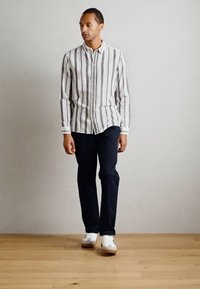 White and gray striped button-up shirt, navy pants, and white sneakers. Features a classic fit with a collar and long sleeves.