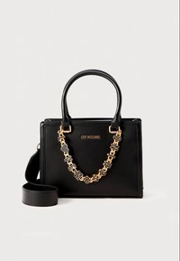 Black faux leather handbag with dual top handles, gold chain strap featuring letter accents, and embossed logo on the front.