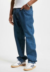 Blauwe denim jeans met een losse pasvorm, vijf zakken en zichtbare stiksels; lichtgewicht stof; gecombineerd met witte sneakers met grijze en blauwe accenten.