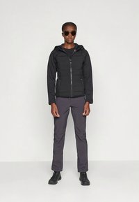 Juodas hoodie su užtrauktuku, pūsto dizaino ir reguliuojama gaubtu, derinamas su tamsiai pilkomis kelnėmis ir juodais batais. Elegantiškas, minimalistinis stilius.