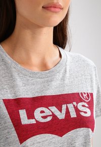 T-shirt en coton gris avec un logo Levi's rouge bien en évidence sur le devant, col rond et manches courtes avec une texture lisse.