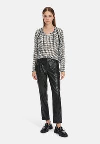 Schwarze und weiße, verkürzte Kapuzenjacke mit Hahnentrittmuster, Kapuze mit Kordelzug, kombiniert mit schwarzen Kunstlederhosen und klobigen schwarzen Loafers.